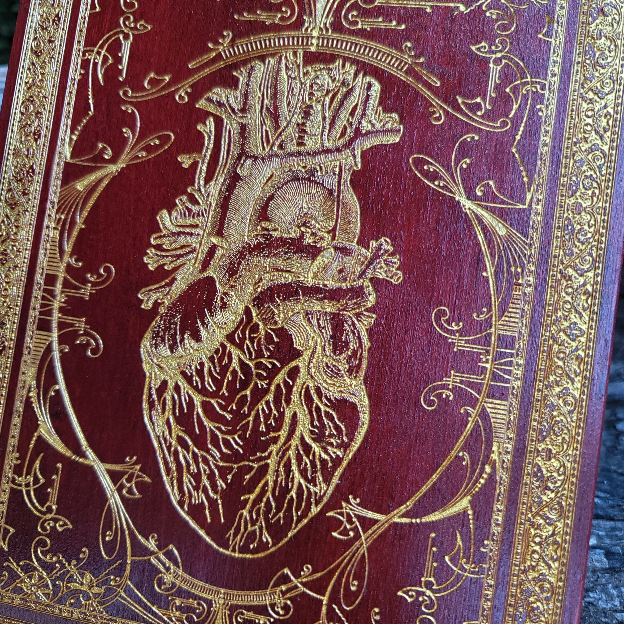 Macabre yet romantic red heart artwork with gold veins, painted on a wooden panel.