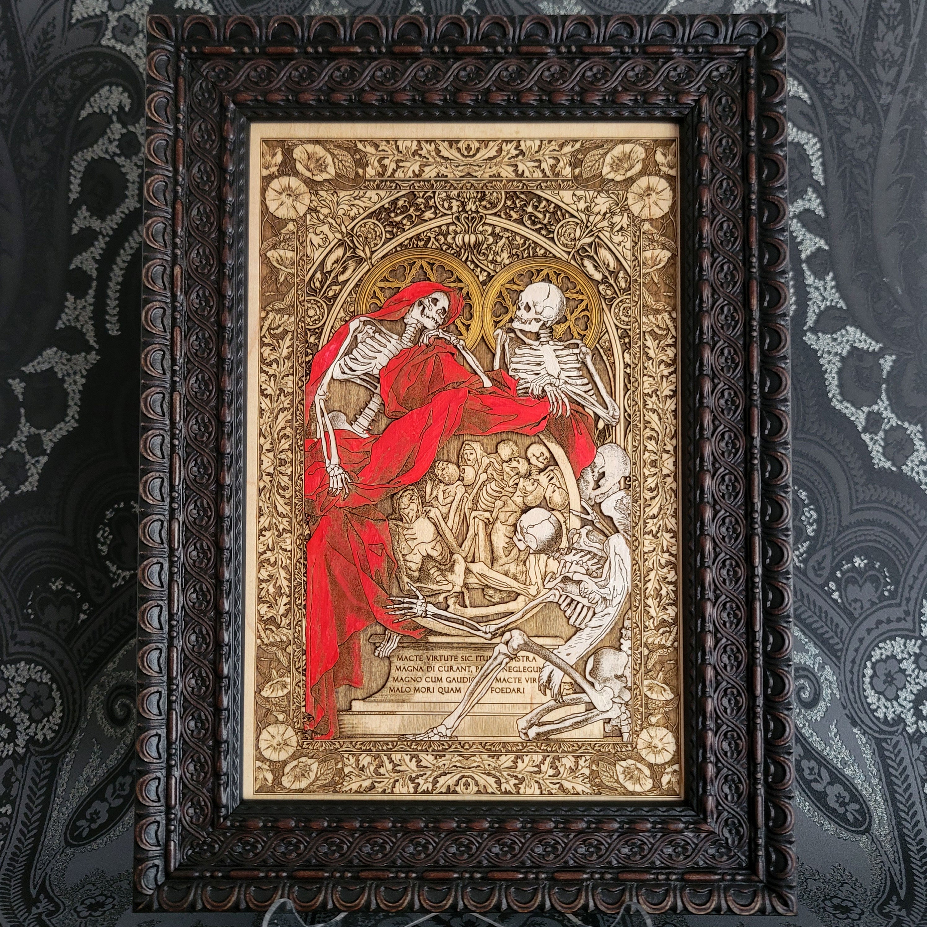 Decorative print of skeletons in a ornate frame on a patterned wall.