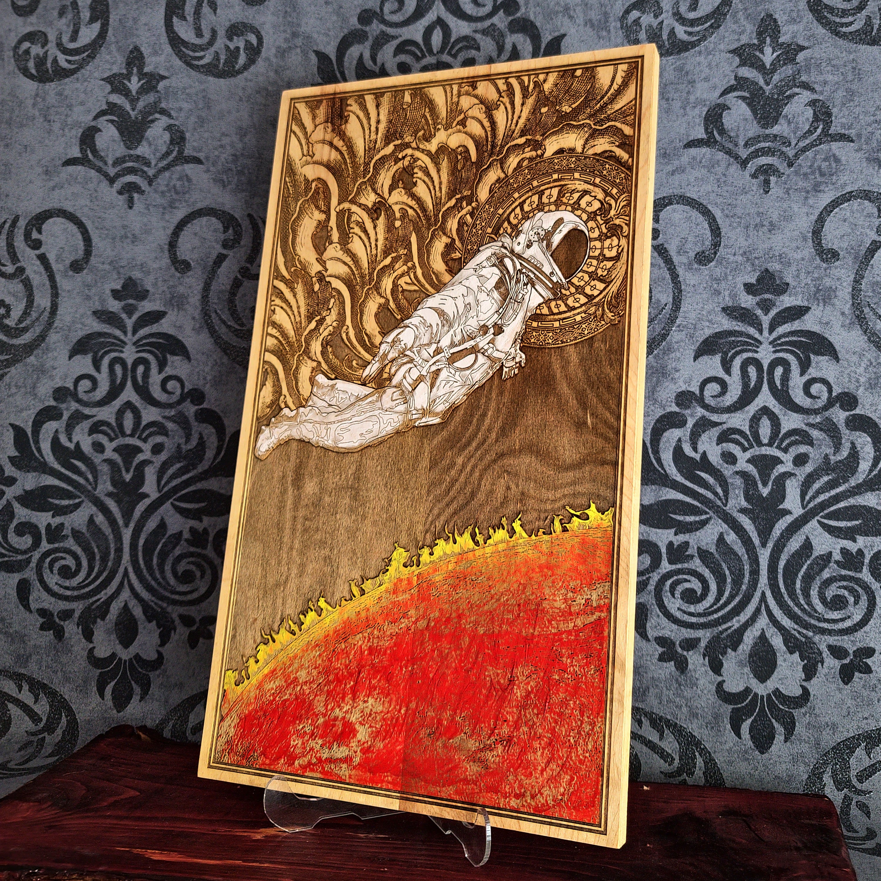 A wood burned artwork depicting an astronaut floating in space above a fiery red planet. The astronaut is wearing a white spacesuit and helmet. The background is a dark brown wood with intricate details.