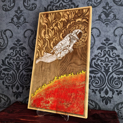 A wood burned artwork depicting an astronaut floating in space above a fiery red planet. The astronaut is wearing a white spacesuit and helmet. The background is a dark brown wood with intricate details.