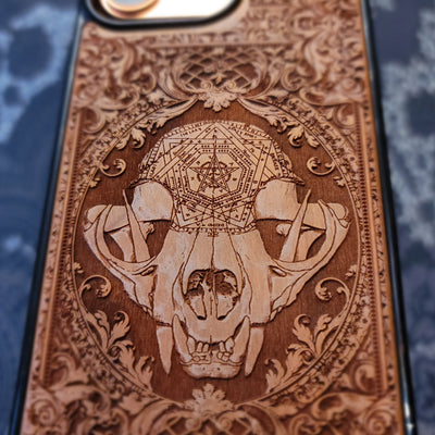 Deep laser engraved wooden phone case featuring a mystical cat skull design with witchy dark art details on natural wood for iPhone and Samsung Galaxy models.