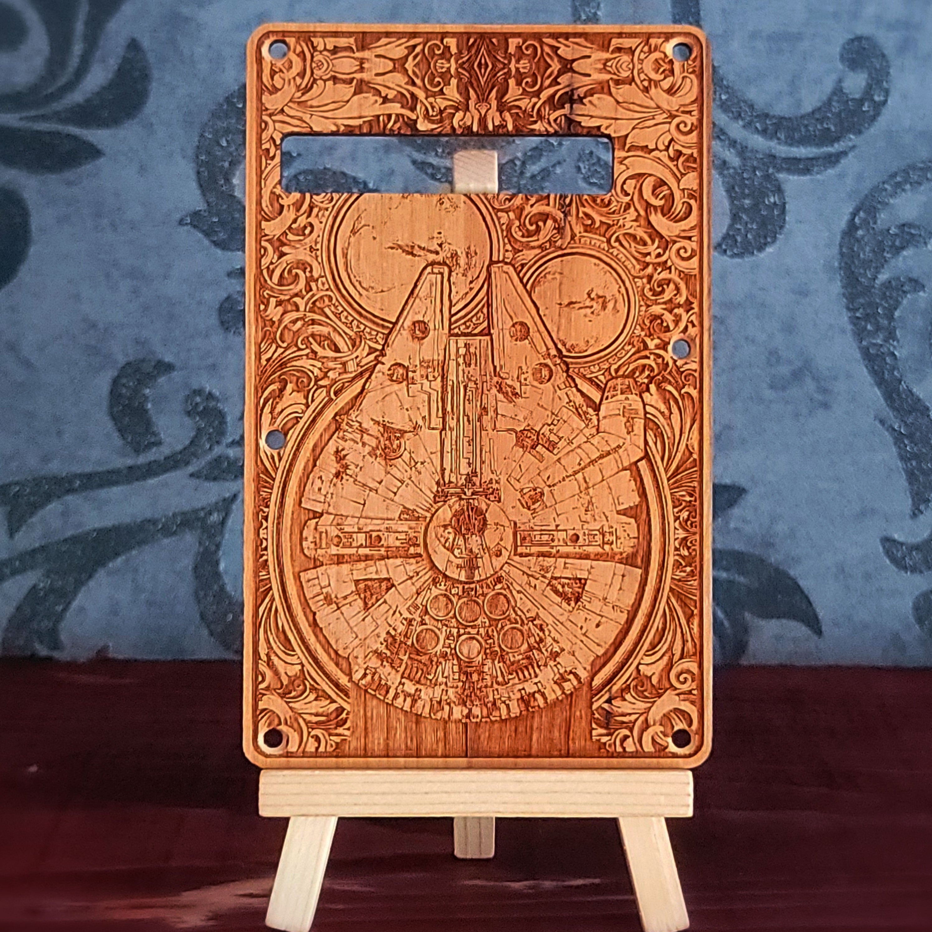 A wooden guitar backplate with a detailed laser-etched design of the mill falcon. The backplate is brown with a light wood grain and has a rectangular shape with rounded corners.