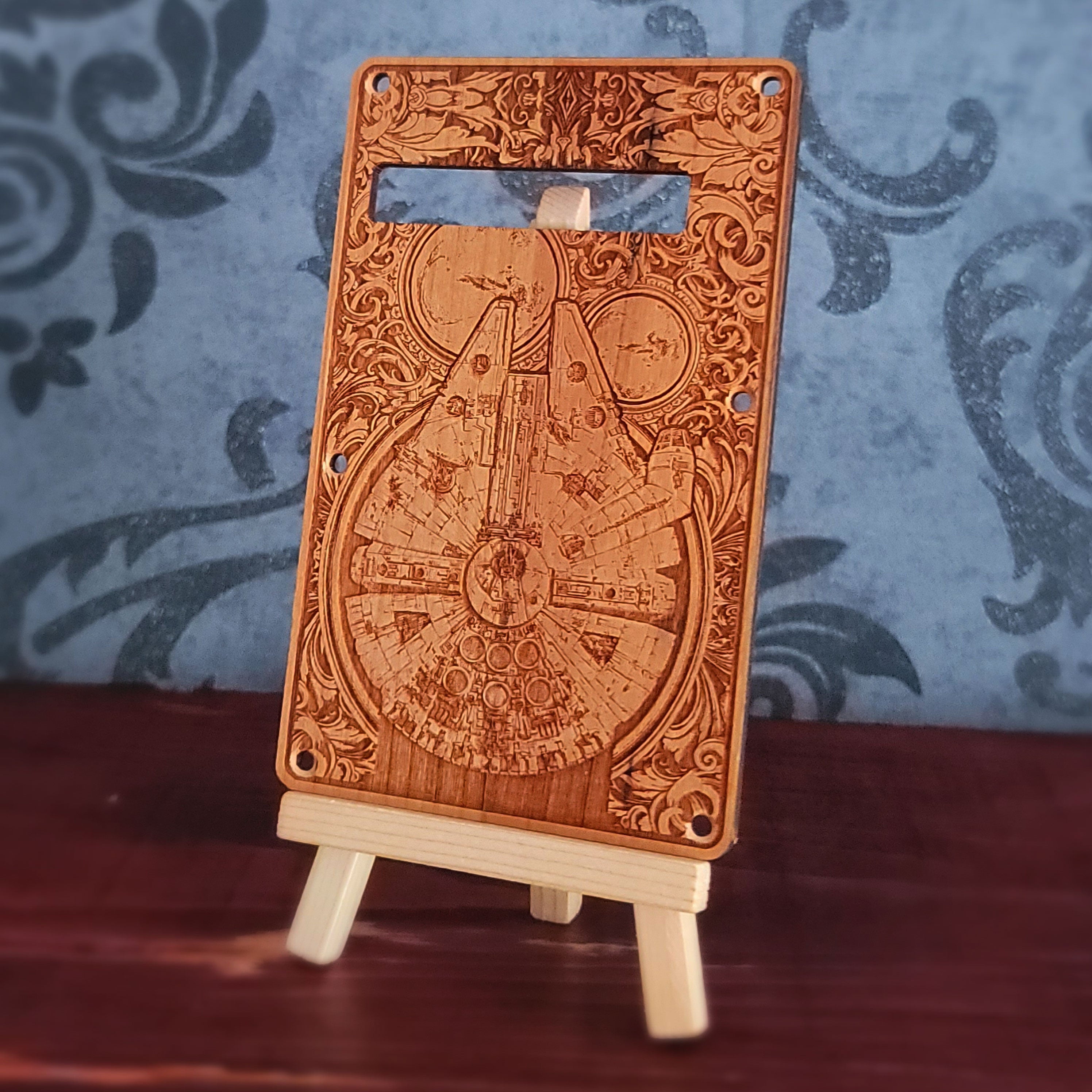 A wooden guitar backplate with a detailed laser-etched design of the mill falcon. The backplate is brown with a light wood grain and has a rectangular shape with rounded corners.