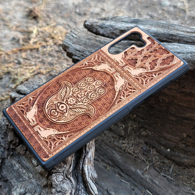 Wooden phone case featuring a beautifully intricate Hamsa hand design, intricately laser-engraved with fine detailing. The design is symbolic of protection, peace, and good fortune. Compatible with iPhone , 15, 14, 13, 12, 11 Pro Max Mini and Samsung Galaxy S, S24, S23, S22, S21, S20 Ultra, Plus, and Note 20. A unique and durable accessory perfect for those seeking a meaningful and stylish phone case.