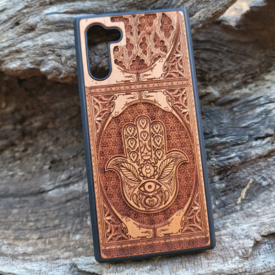 Wooden phone case featuring a beautifully intricate Hamsa hand design, intricately laser-engraved with fine detailing. The design is symbolic of protection, peace, and good fortune. Compatible with iPhone , 15, 14, 13, 12, 11 Pro Max Mini and Samsung Galaxy S, S24, S23, S22, S21, S20 Ultra, Plus, and Note 20. A unique and durable accessory perfect for those seeking a meaningful and stylish phone case.