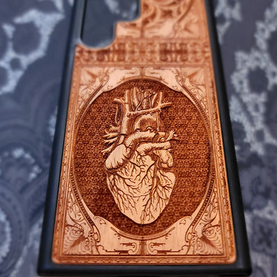 Deep laser engraved wooden phone case featuring an anatomical human heart design on natural wood for iPhone and Samsung Galaxy models.