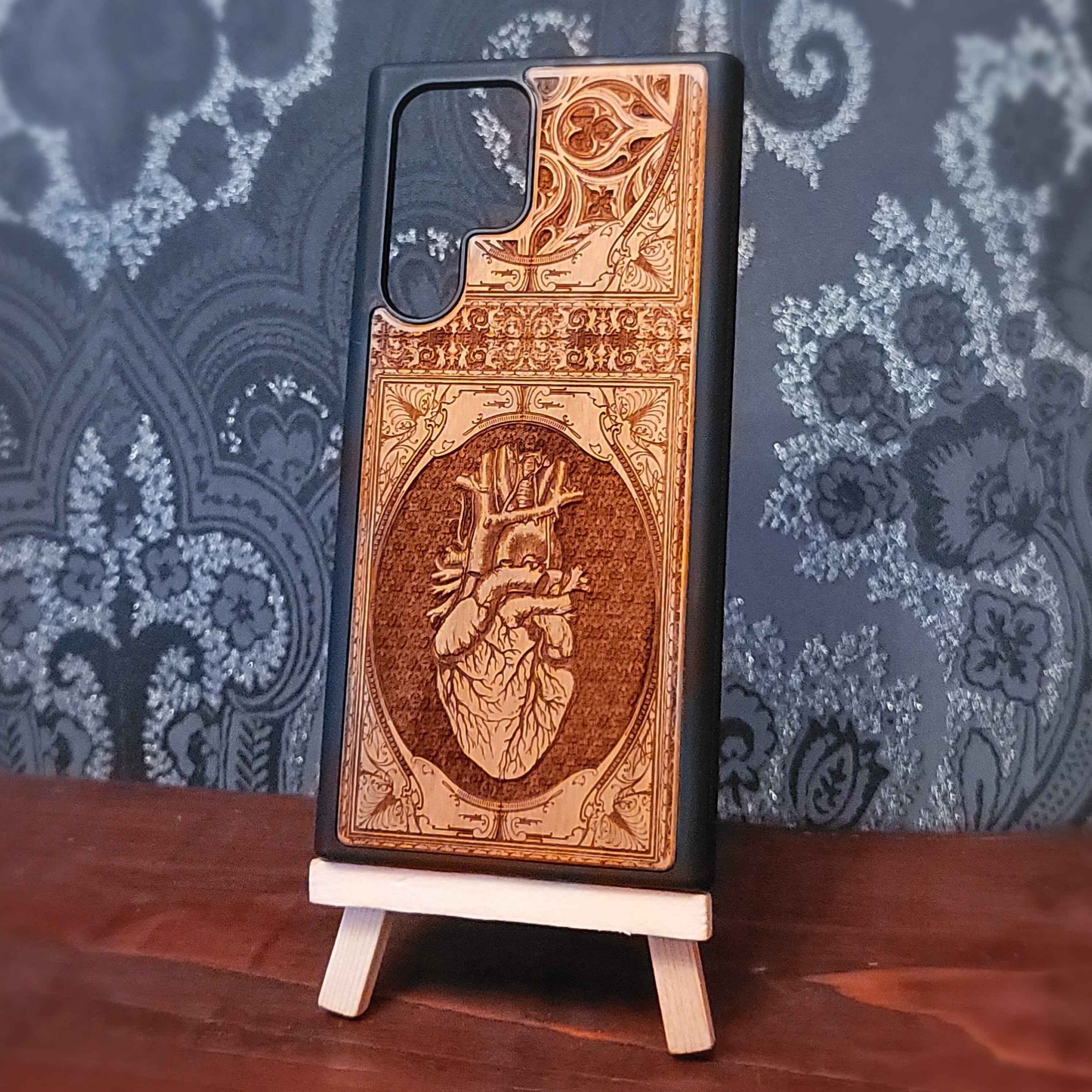 Deep laser engraved wooden phone case featuring an anatomical human heart design on natural wood for iPhone and Samsung Galaxy models.