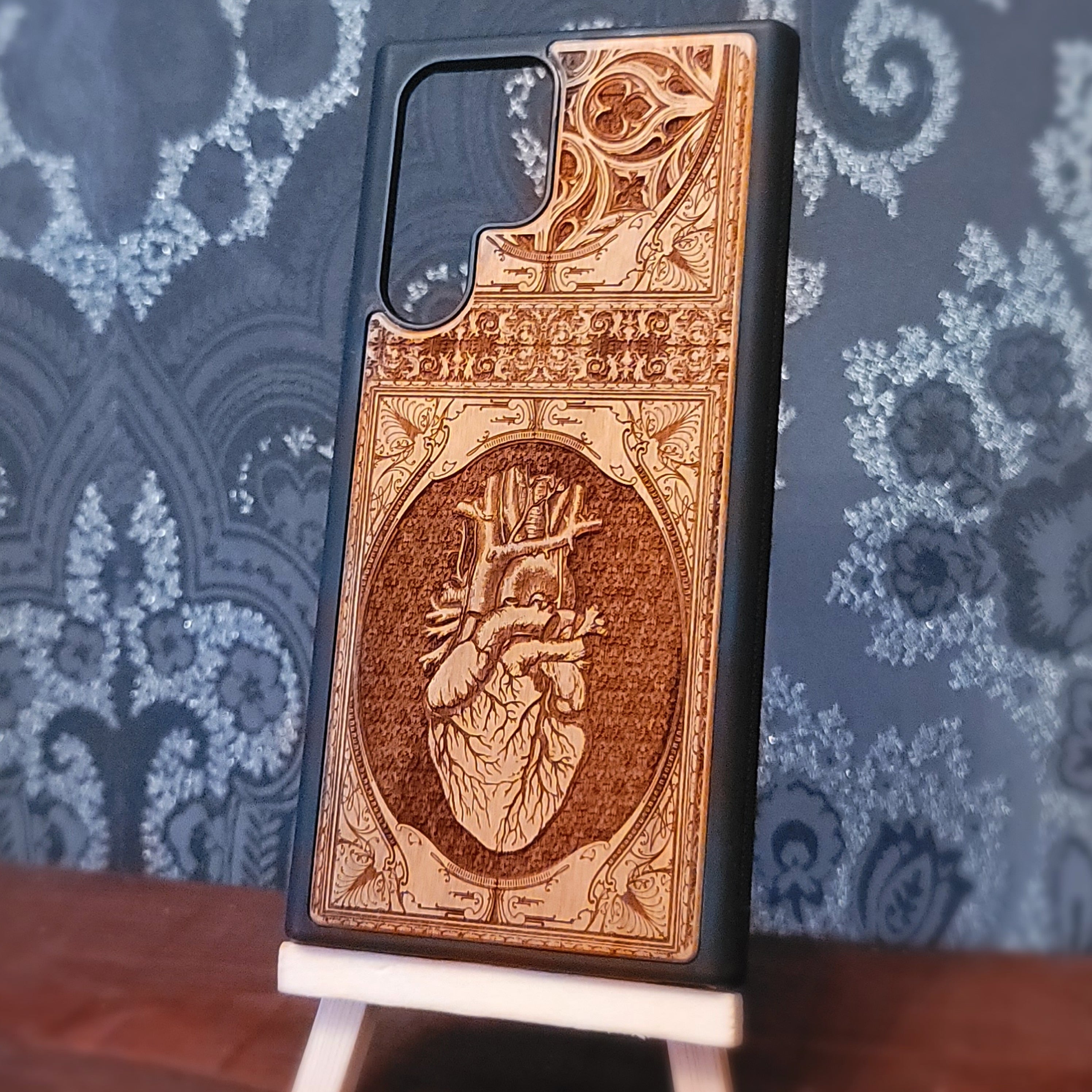 Deep laser engraved wooden phone case featuring an anatomical human heart design on natural wood for iPhone and Samsung Galaxy models.