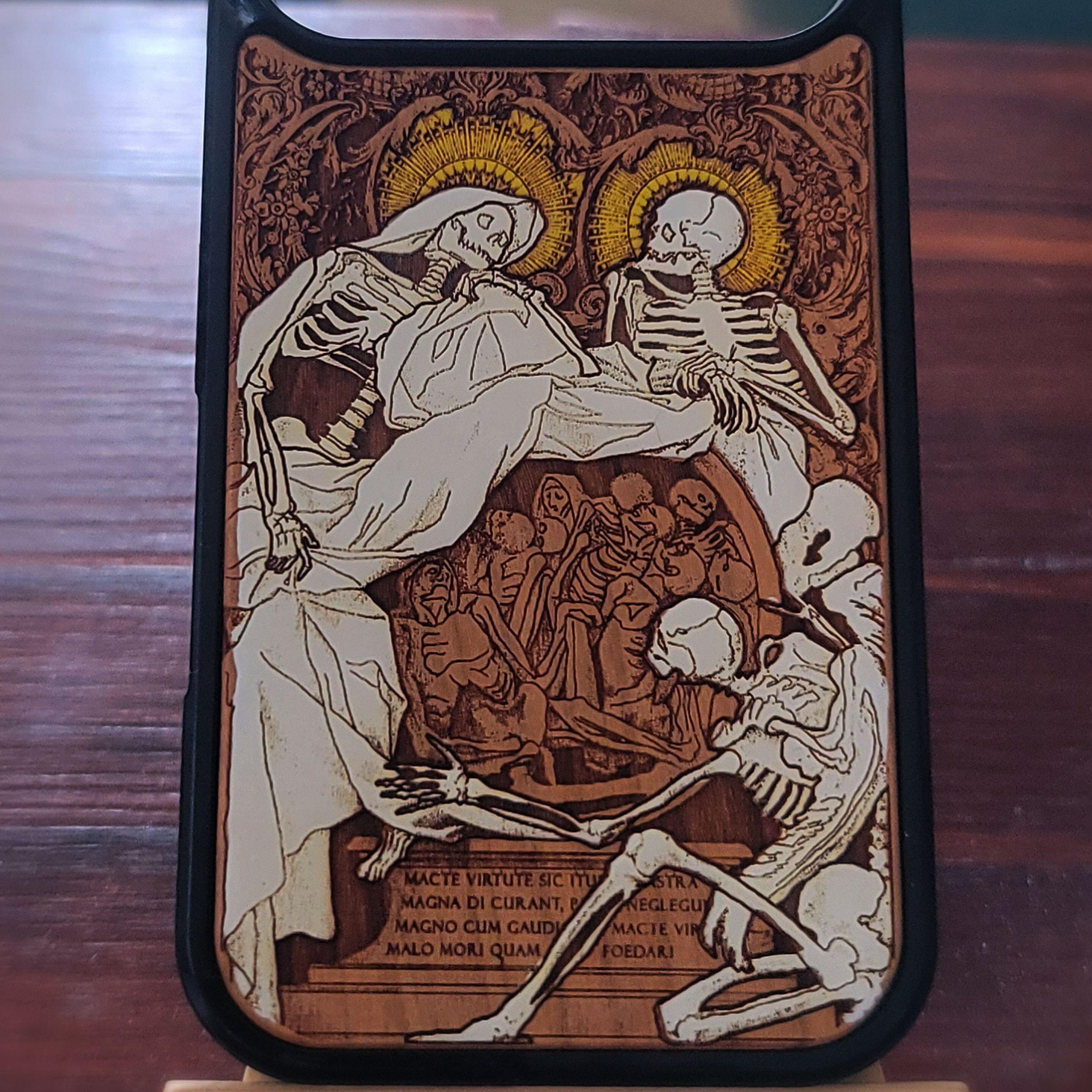 A phone case featuring a detailed medieval-style illustration of two skeletons with gold halos, surrounded by smaller figures and Latin text, shown on a dark wooden surface.
