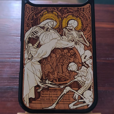 A phone case featuring a detailed medieval-style illustration of two skeletons with gold halos, surrounded by smaller figures and Latin text, shown on a dark wooden surface.
