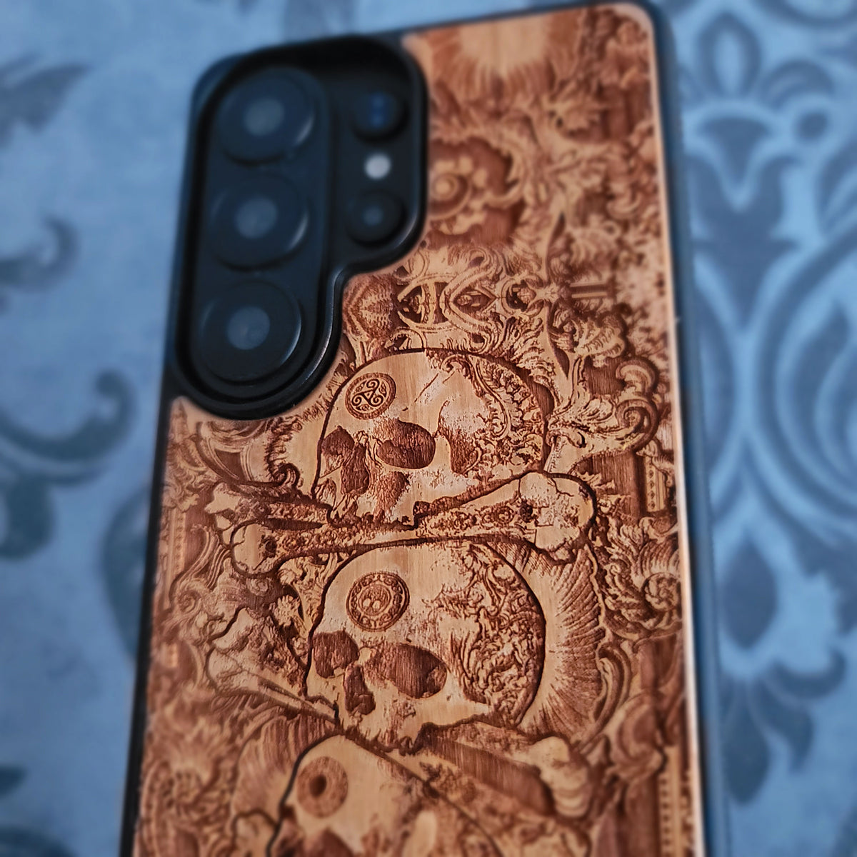 Natural cherrywood phone case featuring detailed stacked skull engraving
