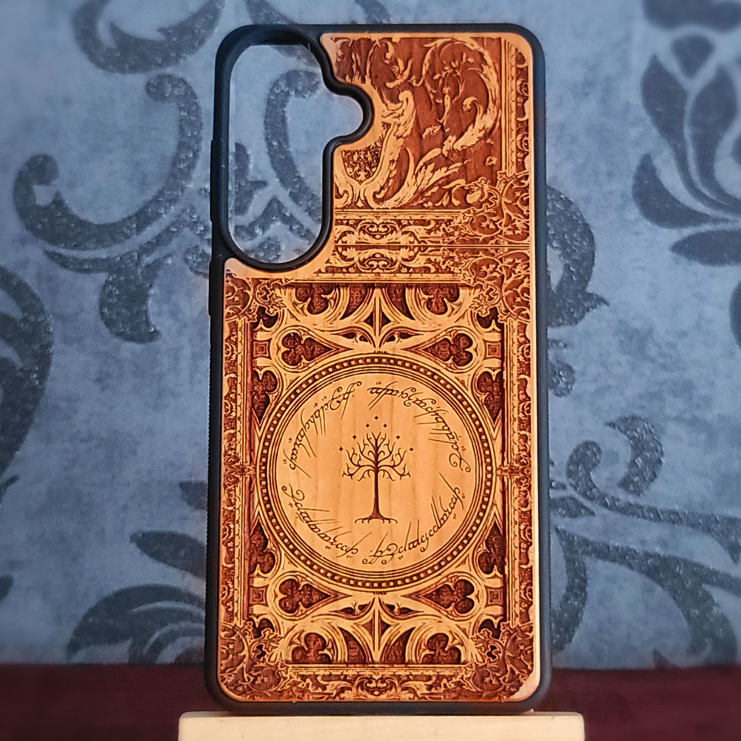 A custom laser-engraved wooden phone case featuring a detailed design inspired by The Lord of the Rings, including the Tree of Gondor in a circular emblem and a winged motif at the top,