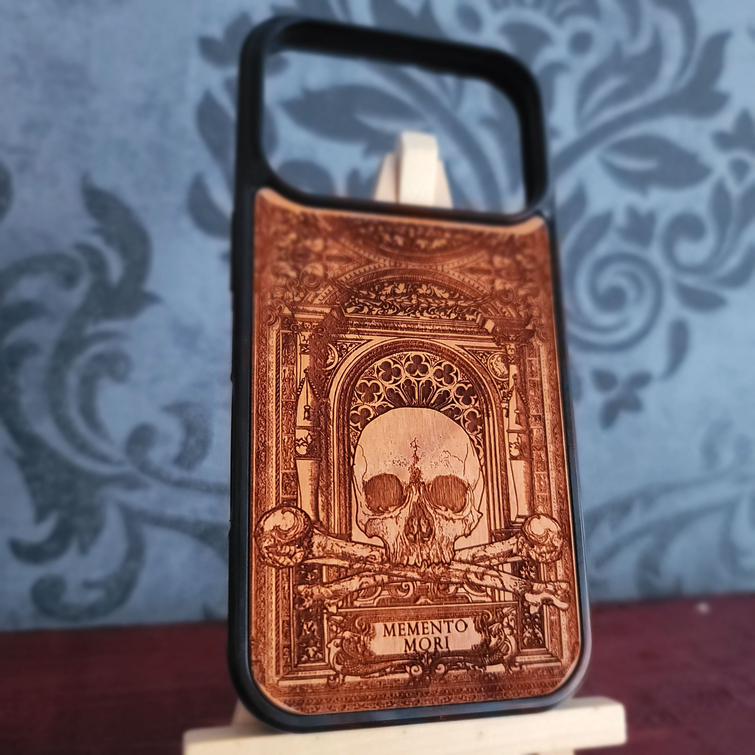 A phone case engraved gothic-style design featuring a skull and the text 'MEMENTO mORI',