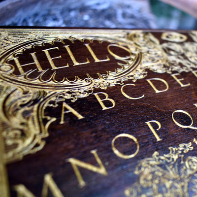 Spirit communication board design on gold-accented dark wood wall art.