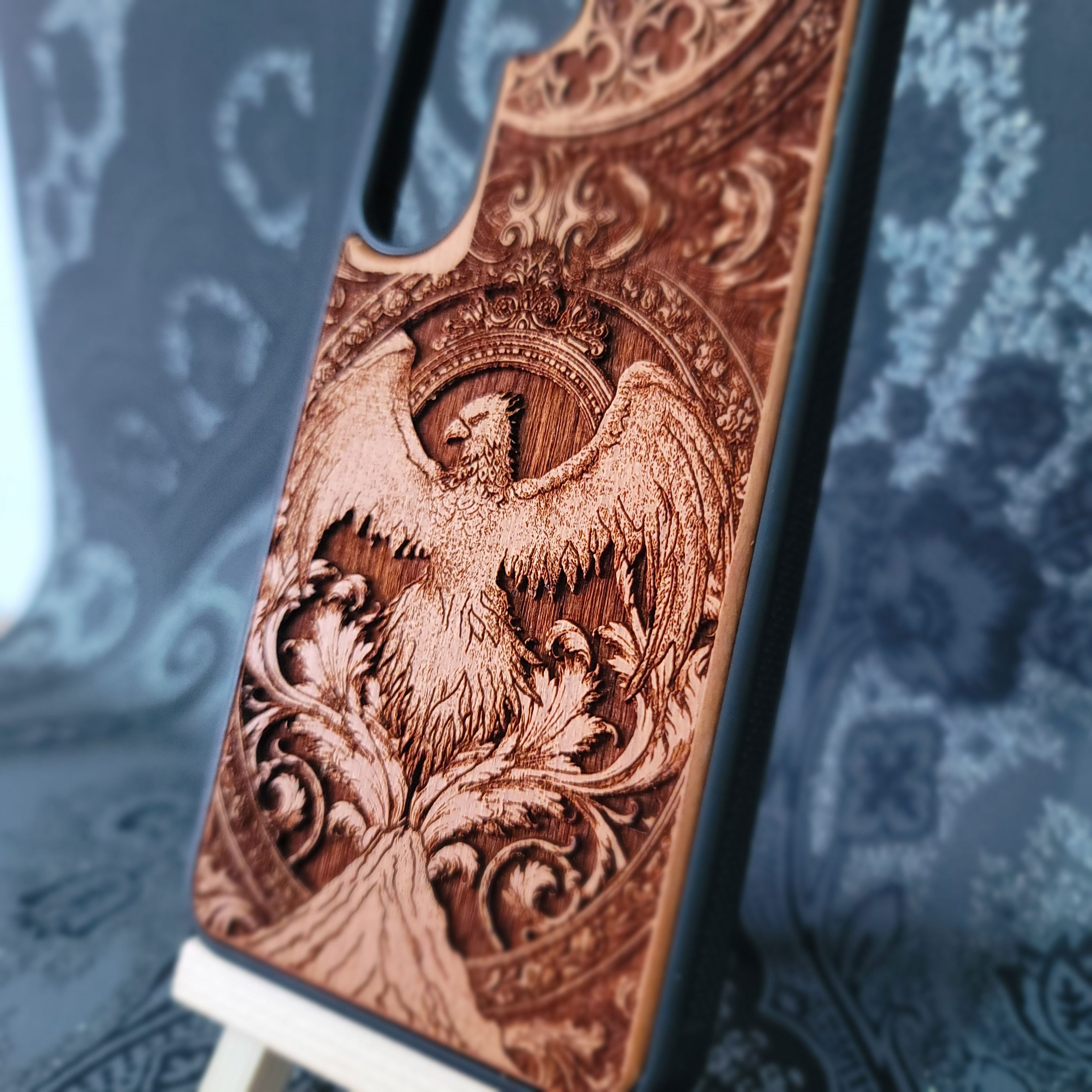 Deep laser engraved wooden phone case featuring a mythical phoenix bird design on natural wood. Available for iPhone and Samsung Galaxy.