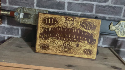 Occult-themed Ouija board artwork on wood with aged gold accents.