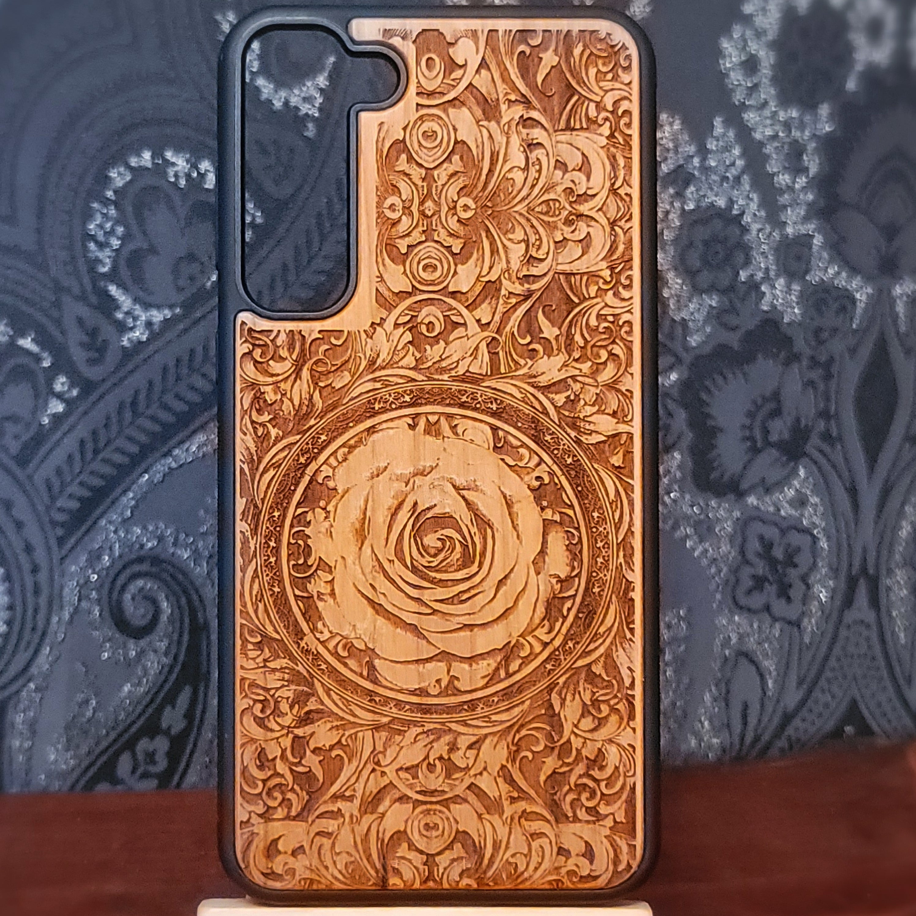 Deep laser engraved wooden phone case featuring an intricate floral design with a large detailed rose on natural wood for iPhone and Samsung Galaxy models.