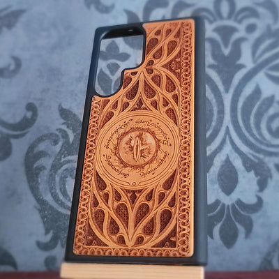 A wooden phone case with an intricate laser-engraved design inspired by The Lord of the Rings, featuring a circular Elvish emblem and script, 