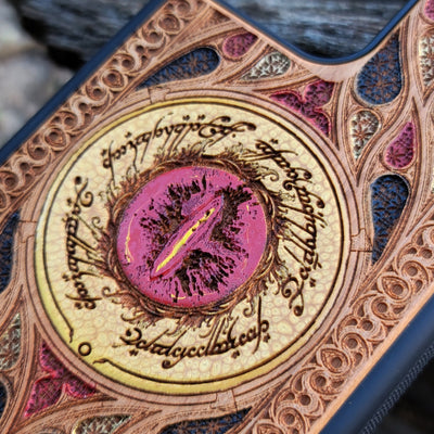 "Hand-painted wood phone case featuring the Eye of Sauron surrounded by intricate Elvish script and vibrant colored patterns. This laser-engraved and detailed design offers a unique blend of artistry and durability. Compatible with iPhone , 15, 14, 13, 12, 11, Pro Max, Mini, and Samsung Galaxy S, S24, S23, S22, S21, S20 Ultra, Plus, Note 20. Perfect for Lord of the Rings fans seeking a bold and protective accessory