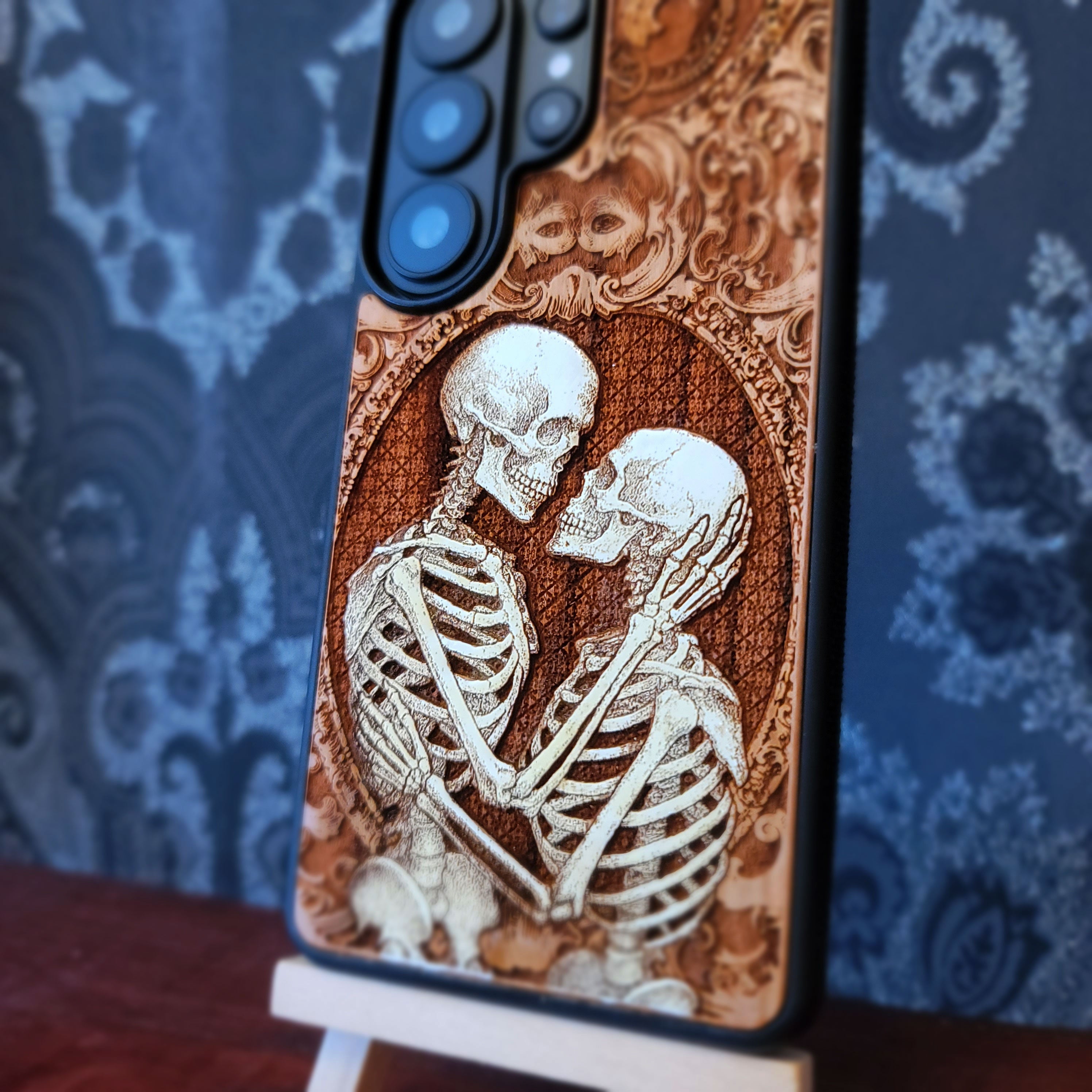 Gothic skeleton couple kissing engraved on wood phone case, romantic dark art design for iPhone 16 & Galaxy S25.