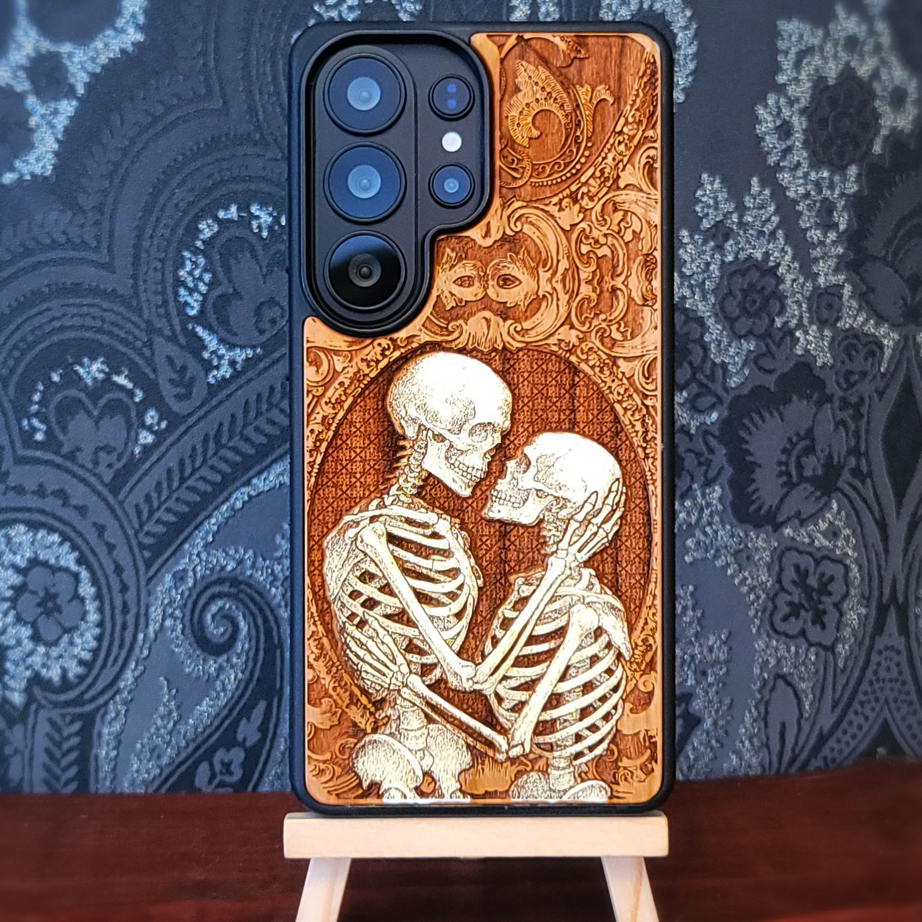 Gothic skeleton couple kissing engraved on wood phone case, romantic dark art design for iPhone 16 & Galaxy S25.