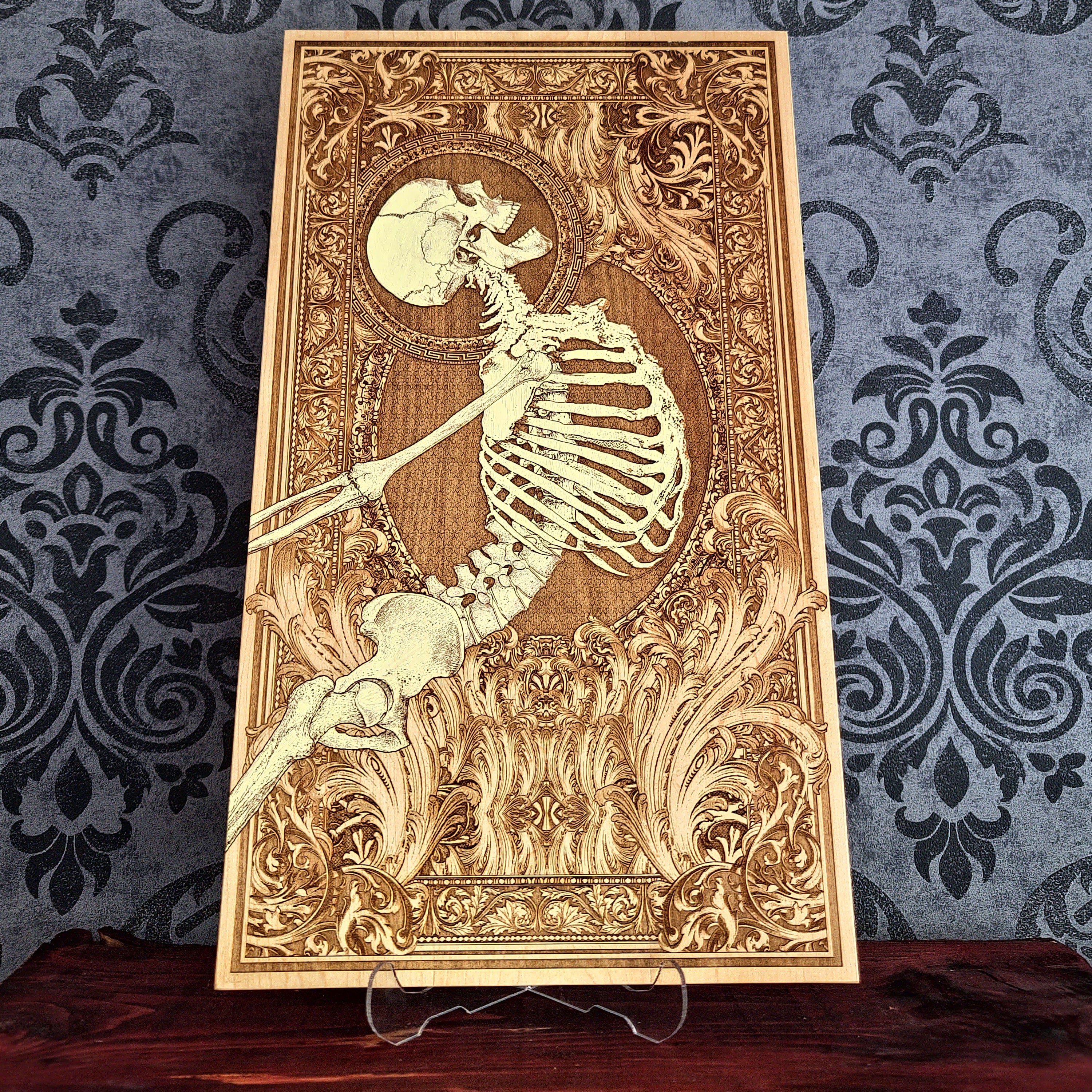 A rectangular wooden wall art plaque featuring a detailed laser-engraved skeleton , set against an ornate baroque-style border. 