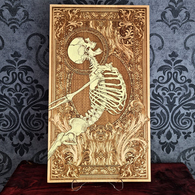 A rectangular wooden wall art plaque featuring a detailed laser-engraved skeleton , set against an ornate baroque-style border. 