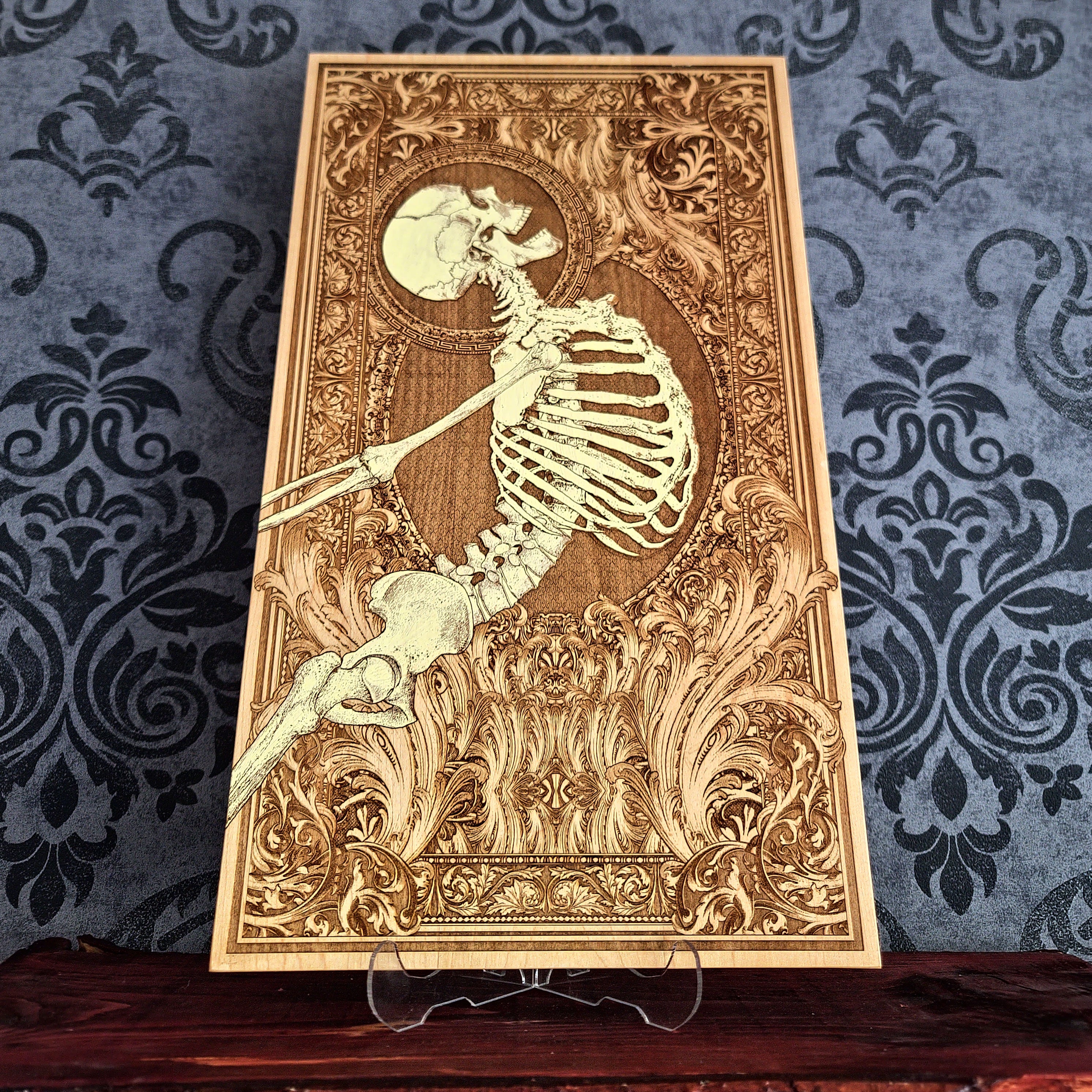 A rectangular wooden wall art plaque featuring a detailed laser-engraved skeleton , set against an ornate baroque-style border. 