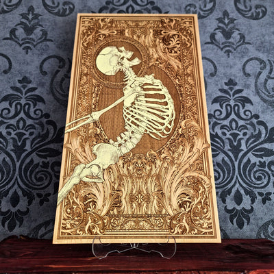 A rectangular wooden wall art plaque featuring a detailed laser-engraved skeleton , set against an ornate baroque-style border. 