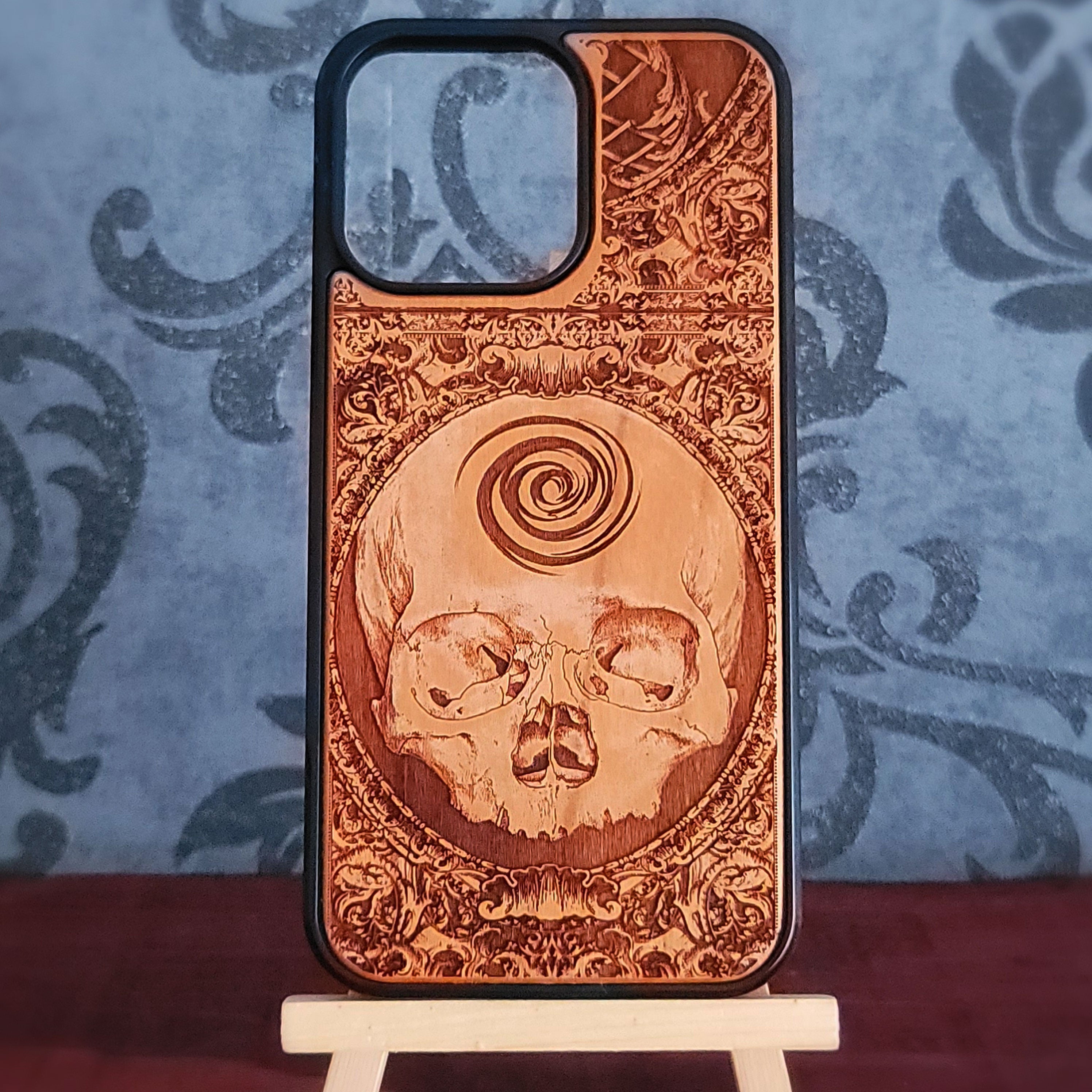 A wooden phone case with a laser-engraved skull and spiral design, 