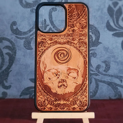 A wooden phone case with a laser-engraved skull and spiral design, 