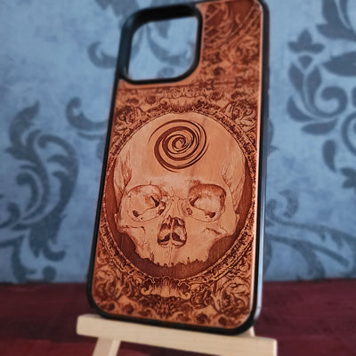A wooden phone case with a laser-engraved skull and spiral design, 