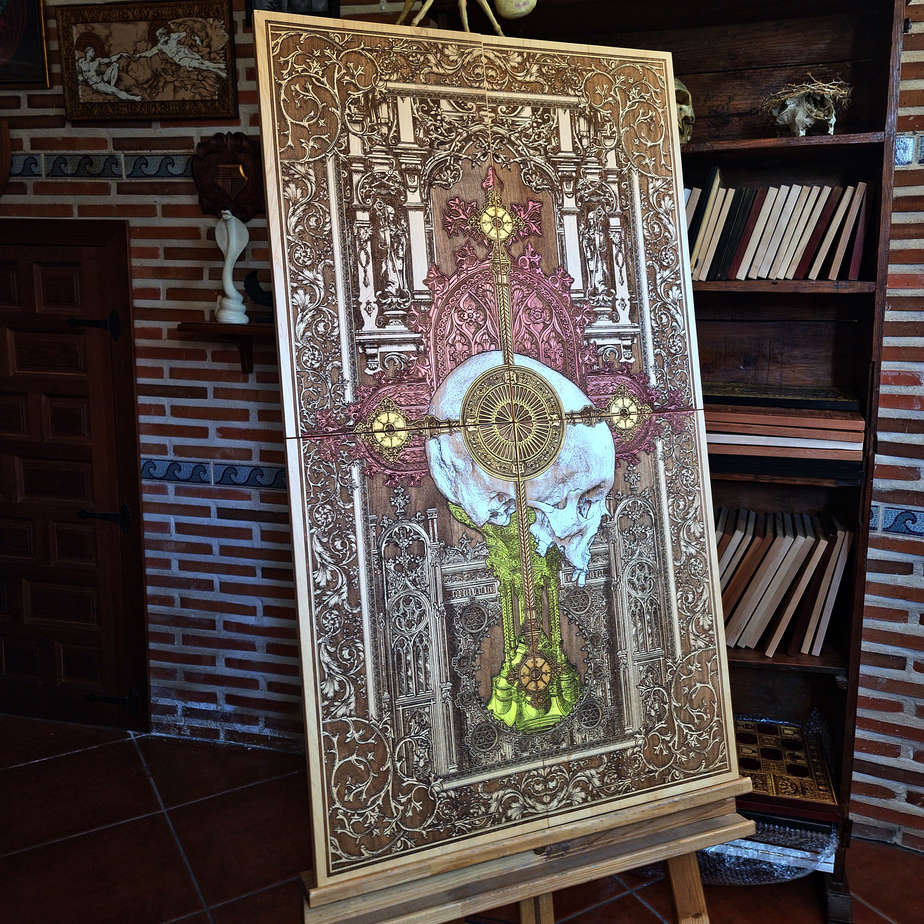 A detailed wooden artwork featuring a skull at the center, overlaid with a cross and intricate gothic architectural elements. The artwork is primarily brown with accents of gold, red, and yellow. 