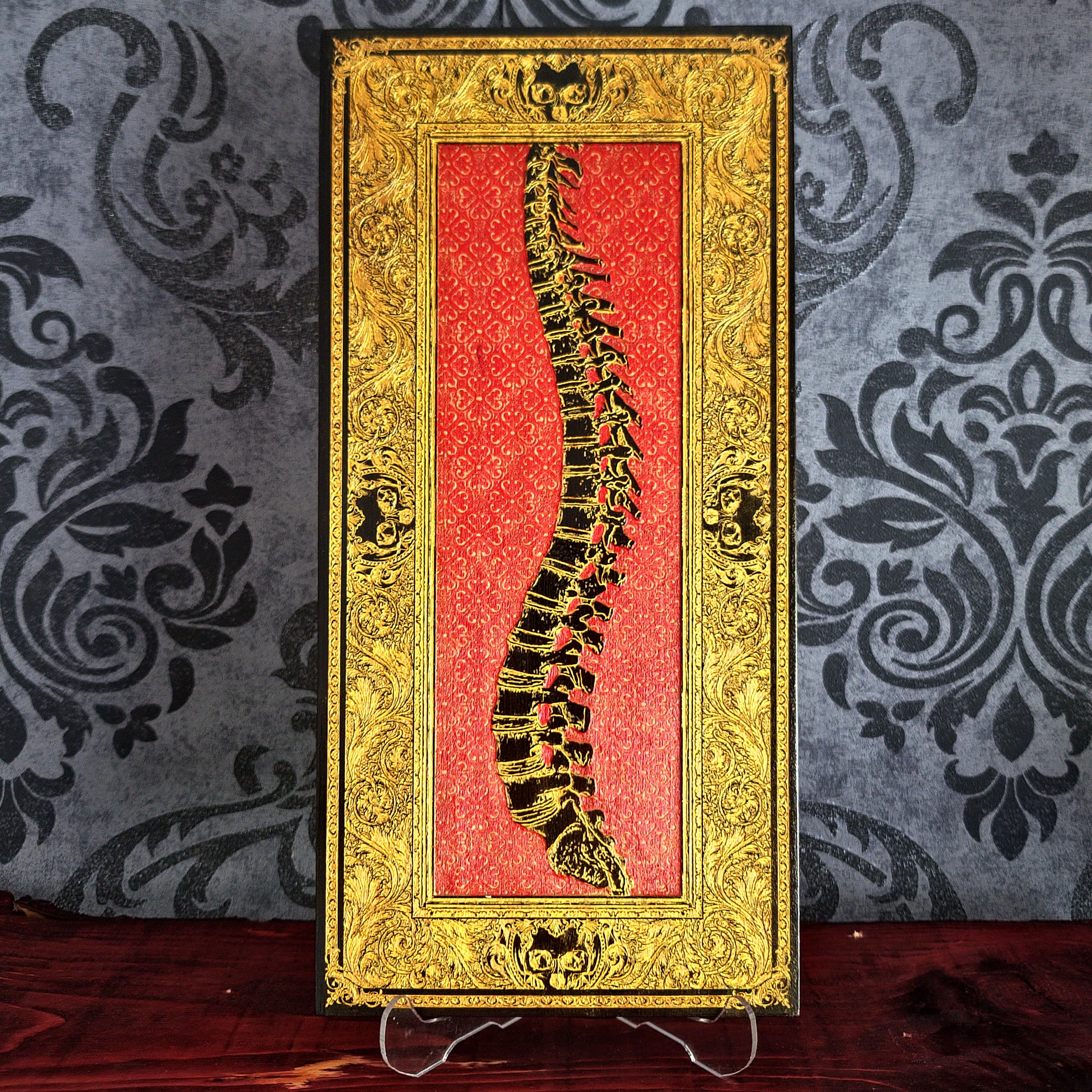 Decorative book with a spine illustration on a red background, framed in gold against a patterned wall.