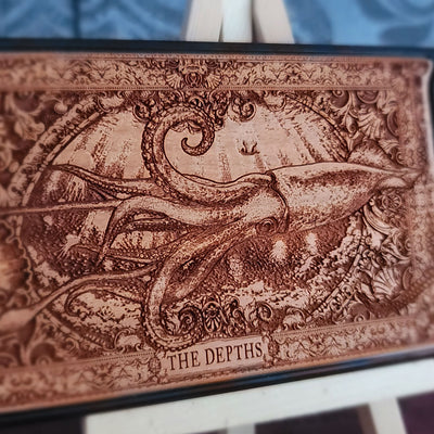 A wood phone case featuring a detailed engraved octopus scene with the text 'THE DEPTHS' at the bottom,