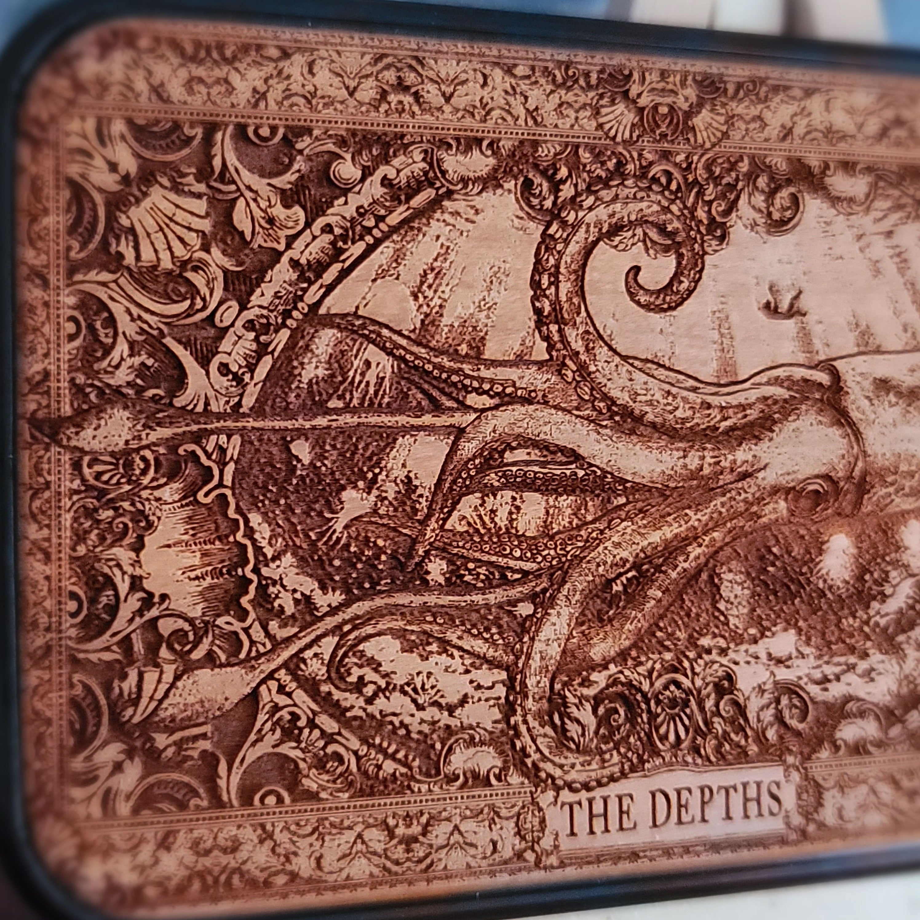 A wood phone case featuring a detailed engraved octopus scene with the text 'THE DEPTHS' at the bottom,
