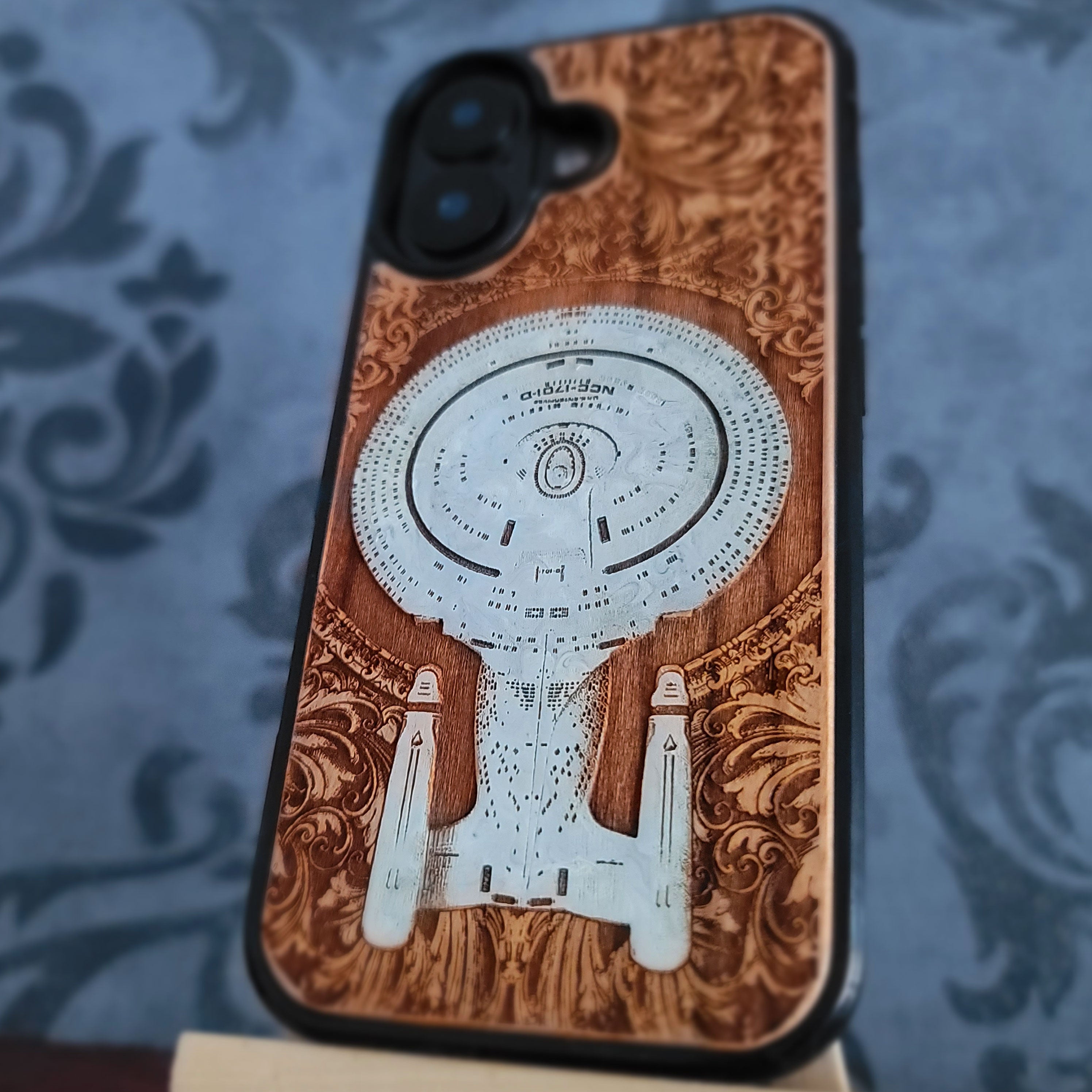 Enterprise NCC-1701-D hand-painted cherrywood phone case, diagonal view highlighting the wood grain and black bumper