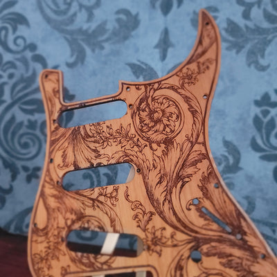 Wooden guitar pickguard with intricate carvings on a blue patterned background