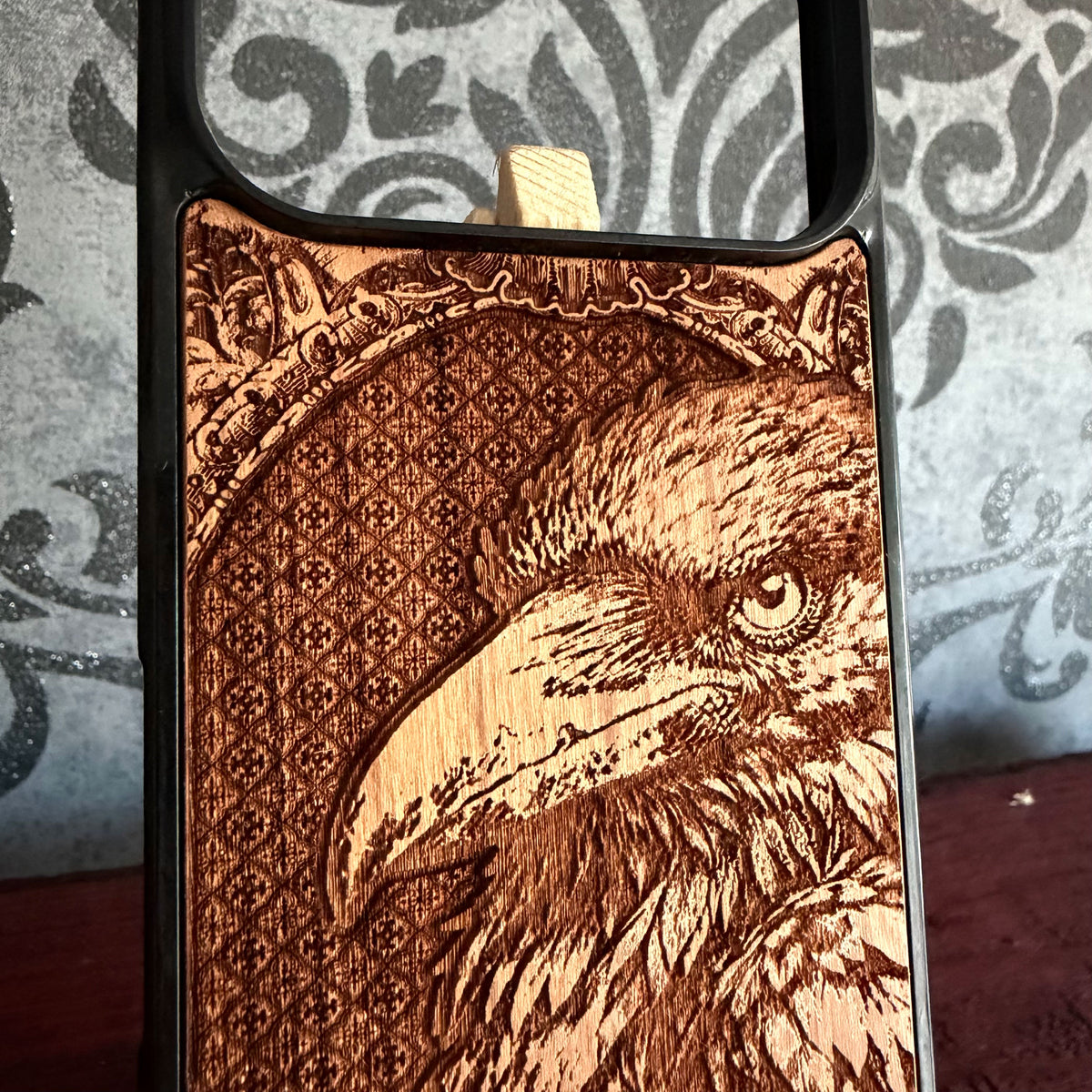 Close up raven portrait engraved into real wood phone case with vintage ornamental border