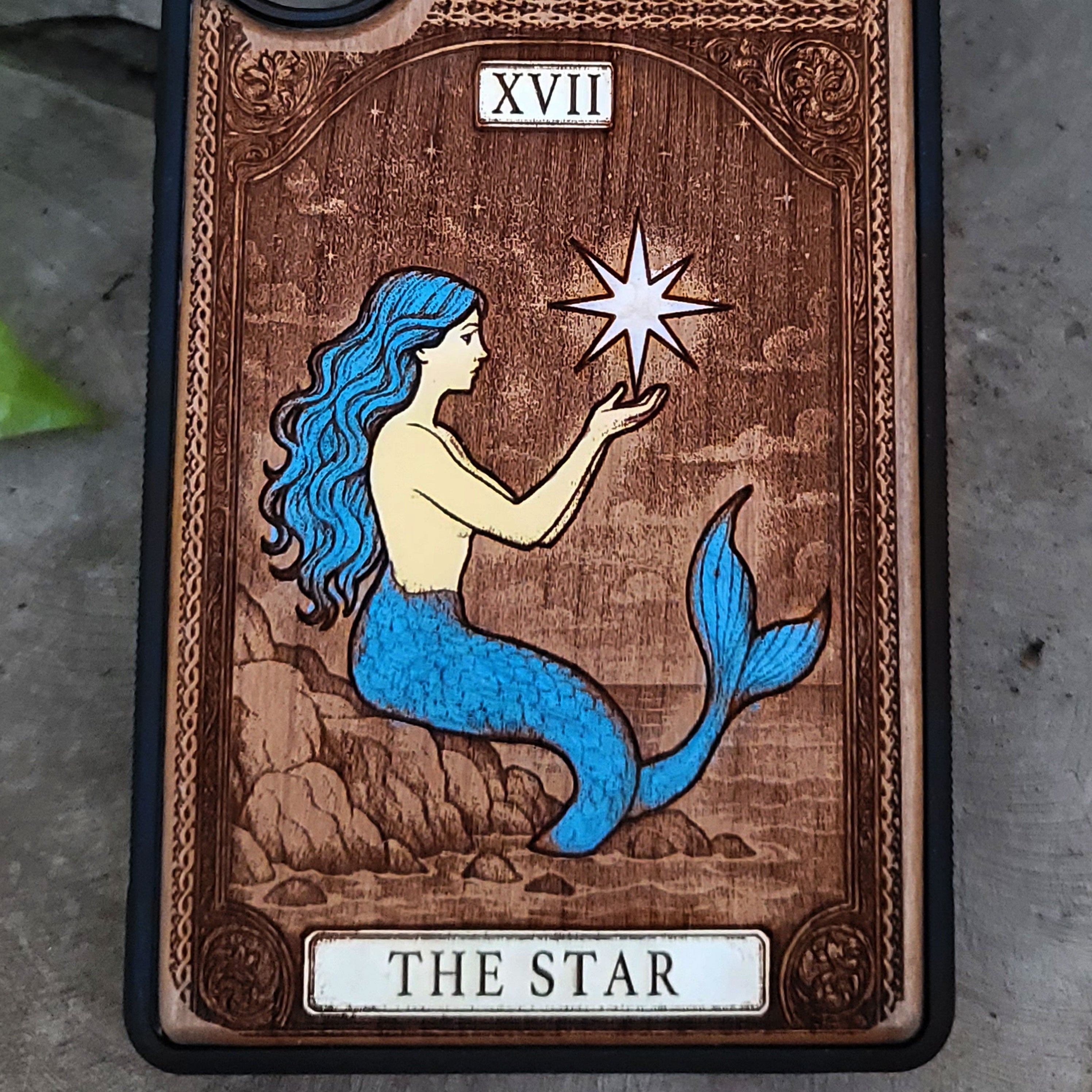 Phone case with mermaid design and 'The Star' tarot card symbolism on a wooden background.