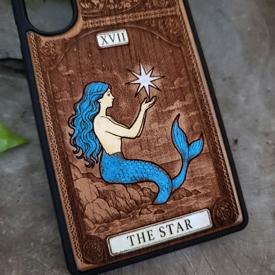 Phone case with mermaid design and 'The Star' tarot card symbolism on a wooden background.
