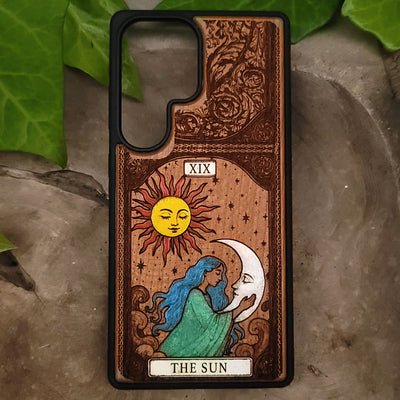 Phone case with sun and moon design and 'The Sun' tarot card illustration on a natural background.