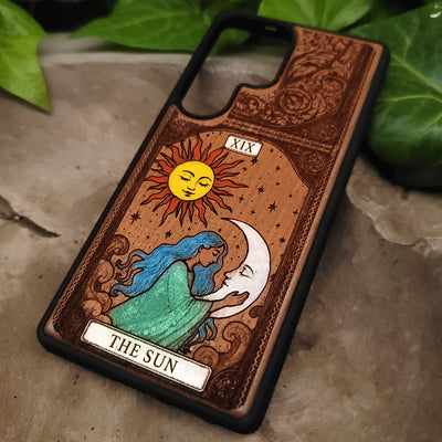 Phone case with sun and moon design and 'The Sun' tarot card illustration on a natural background.
