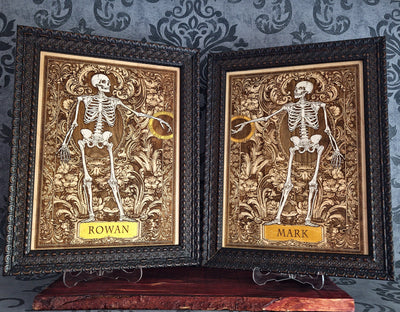 Two framed gothic-style name plates featuring embossed skeletons on ornate gold and brown backgrounds, 
