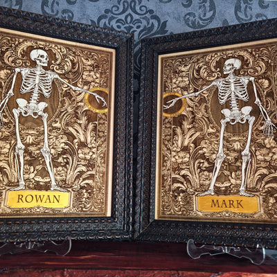 Two framed gothic-style skeleton art prints with ornate gold and brown baroque backgrounds,
