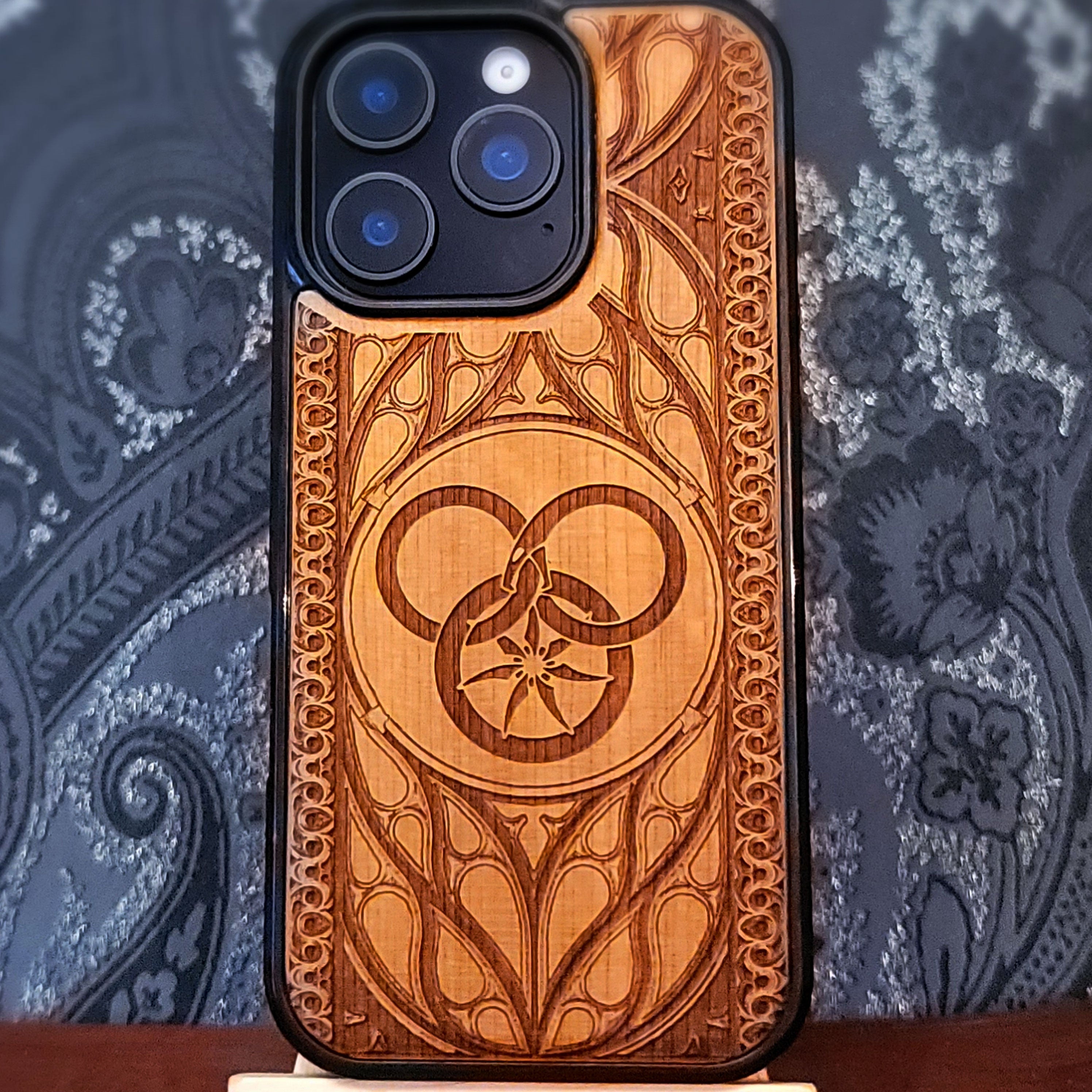 Deep laser engraved wooden phone case featuring a Wheel of Time inspired fantasy symbol on natural wood for iPhone and Samsung Galaxy models.