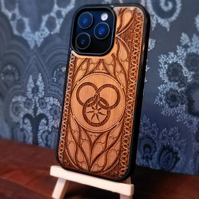 Deep laser engraved wooden phone case featuring a Wheel of Time inspired fantasy symbol on natural wood for iPhone and Samsung Galaxy models.