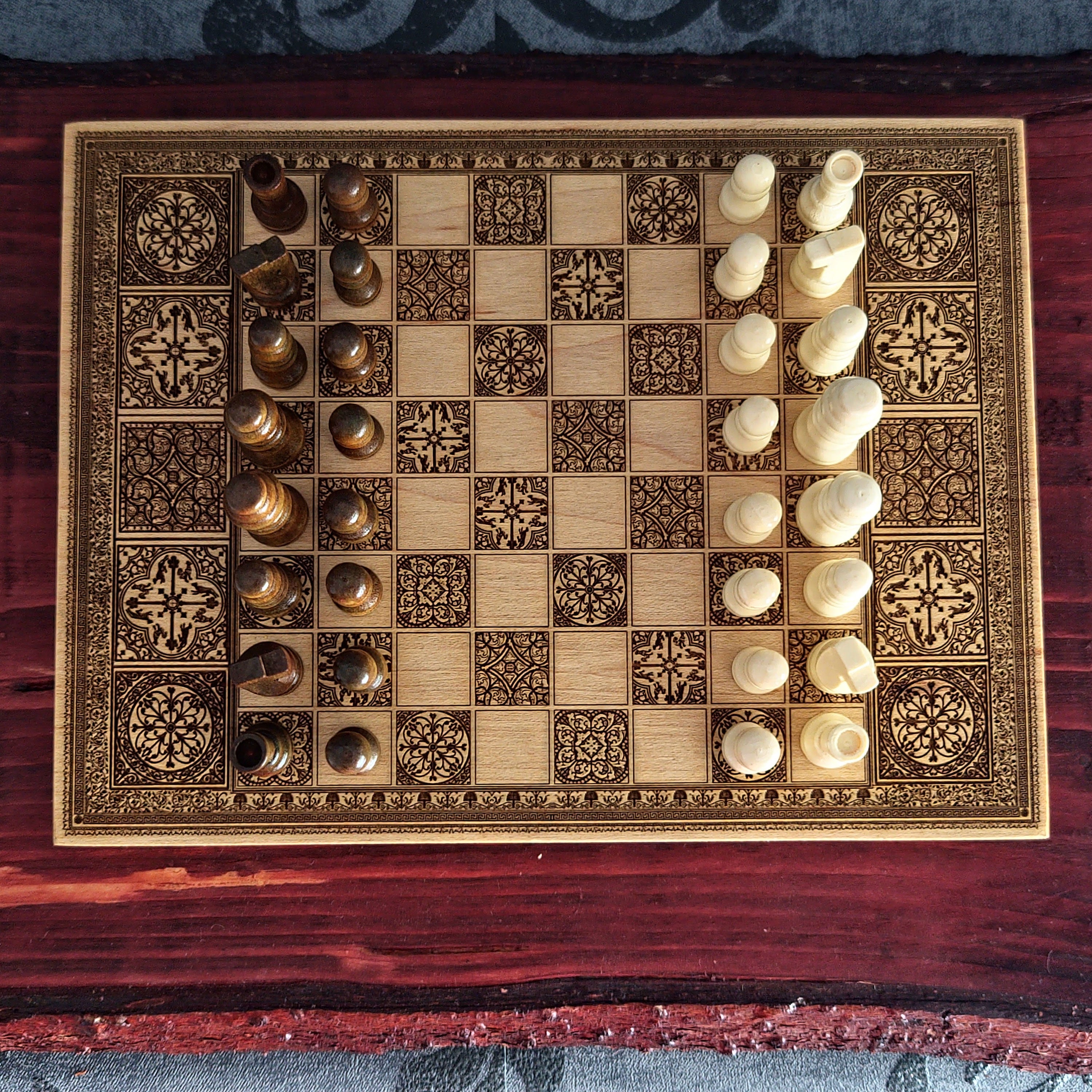 An ornate wooden chessboard with engraved dark brown patterns and matching chess pieces,