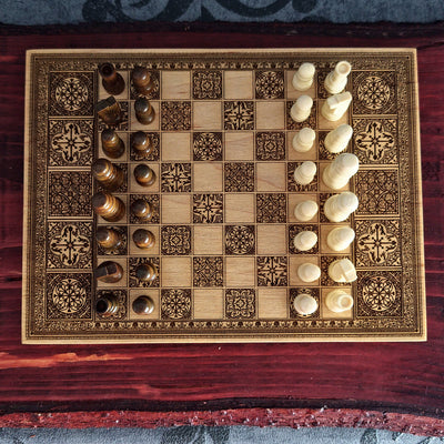 An ornate wooden chessboard with engraved dark brown patterns and matching chess pieces,