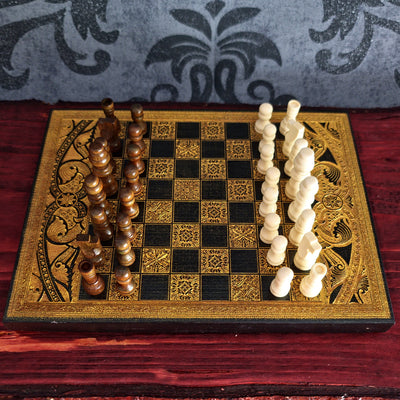 An ornate wooden chessboard with black and gold checkers and carved ivory and brown chess pieces, 
